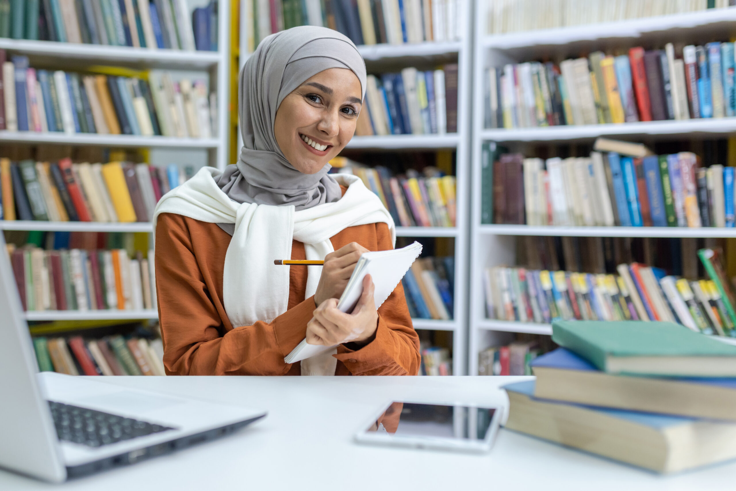 Smiling hijab-wearing student studying in library with laptop